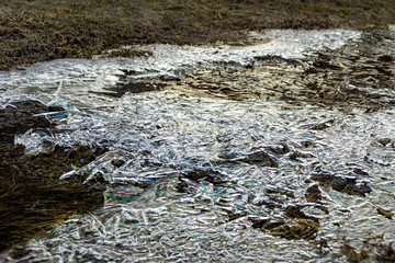 the ice surface of the spring stream is covered with motor vehicle waste, selective focus