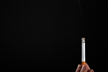 lit cigarette in hand on a black background copy space