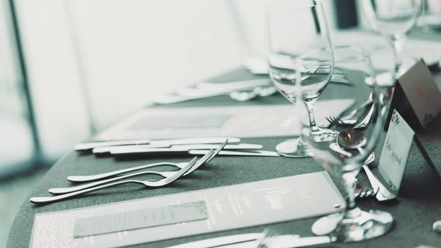 Beautiful table serving, cutlery, on the round table and the guest name tablets and table numbes in the fancy restaurant prepared for the celebrating dinner in minimalistic style in pale green color
