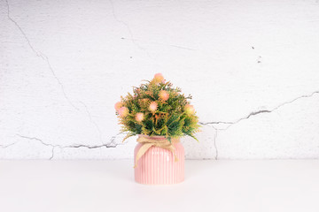 Artifical tropical flower in the ceramic pot in front of stone wall. Table decoration concept