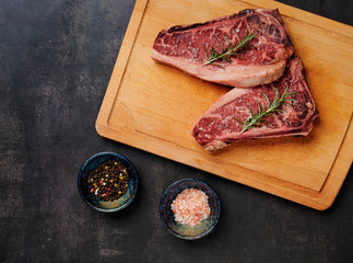 Raw Dry Aged Beef Steak. Raw Dry Aged Meat. Raw sirloin steak on a wooden board with four peppers blend, himalayan salt, and rosemary. black slate stone background