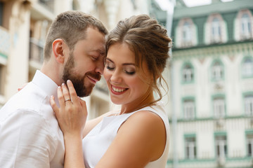 Fototapeta premium Young Bride and Groom couple in summer old City buildings. Tender holding each other. woman & man couple. Romantic date of young happy family near hydrangea bush. lovers newlyweds street style wedding