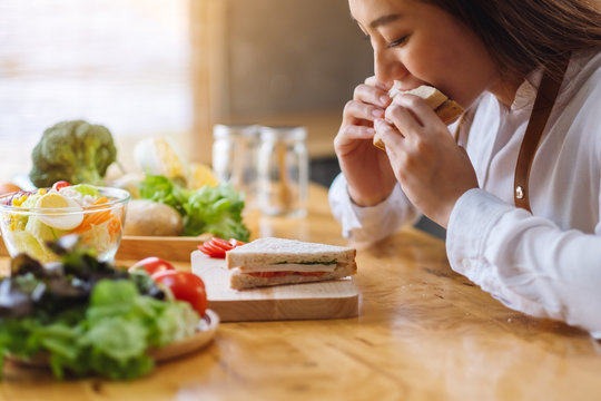 Closeup image of a female chef cooking and eating a whole wheat sandwich in kitchen