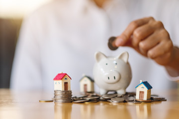 A woman putting coins into piggy bank with house models on pile of coins for saving money concept
