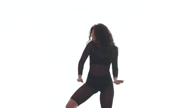 Medium long shot of young beautiful woman in a black transparent tight suit energetically dancing dancehall, street dance, twerk against white background,  isolated