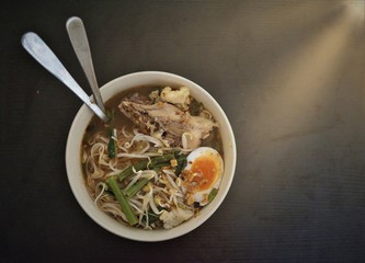  Noodle have sunshine light right conner with egg ,vegetable ,Pork skeleton beef,spoon ,fork in green bowl and  black wood background with clipping path.Spicy noodle. Still life.nodle thailand food.