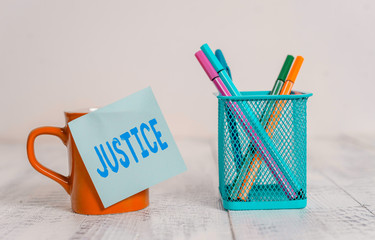Word writing text Justice. Business photo showcasing Quality of being just impartial or fair Administration of law rules Coffee cup mug hot drinks blank sticky note pens metal holder wooden table