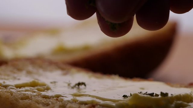 Hand sprinkling oregano or dry herb into garlic butter bread in slow motion
