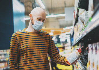 Obraz premium Bald man in medical face mask chooses products in supermarket, concept of coronavirus quarantine
