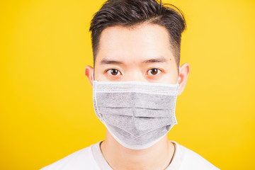 Closeup Asian young man wearing face mask protective germ virus or air dust, studio shot isolated on yellow background and copy space, medical outbreak coronavirus COVID-19 concept