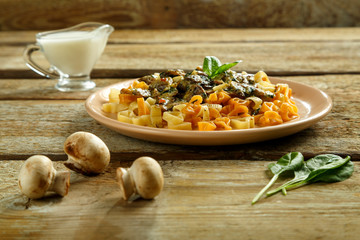 Pasta with mushrooms in a creamy sauce with spinach on a wooden table, mushrooms and milk and greens nearby. Copy space.