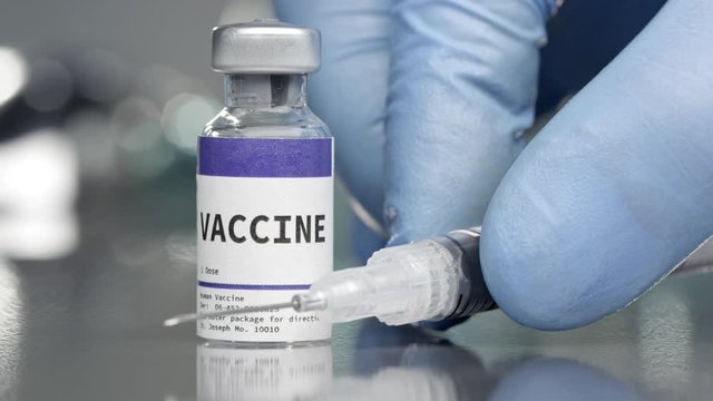 Vaccine vial in medical lab with syringe placed next to it.