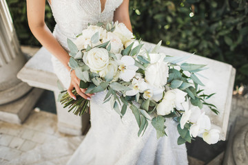 Bride holding in hands elegant blooming bouquet on wedding ceremony. White roses, orchids and greens close up.