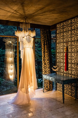 Elegant wedding dress hanging indoors on amazing vintage chandelier. Beautiful warm light.