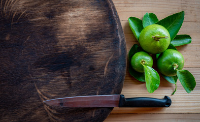  kitchen knife and green lemon on wood cutting board.