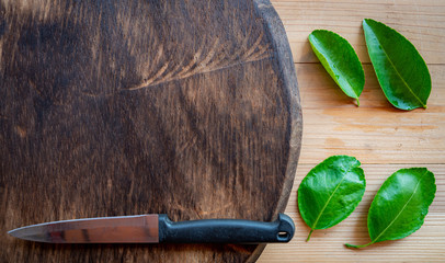 kitchen knife and green lemon leaf on wood cutting board.