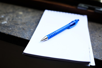 Close up of Dark blue pen and white clear paper note on dark marble window sill. Fixture of open frame behind. Working business kit ready to work at home. Daylight, soft focus