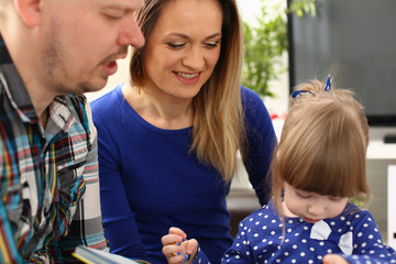 Happy parents with daughter at sofa at home. Beautiful smiling woman and handsome man play with cute little girl childhood and parenthood concept