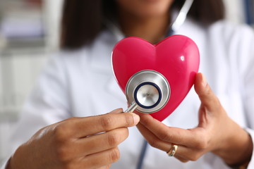 Beautiful black smiling female doctor hold in arms red toy heart closeup. Cardio therapeutist...