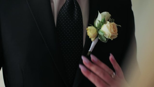 a man in a jacket hangs a white buttonhole of a rose