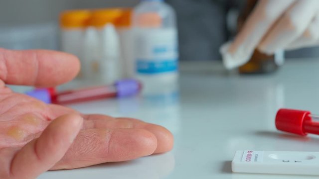 blood sampling and capillary blood test. nurses hand in protective glove disinfects patients finger and pricking it for blood sampling to rapid test for viral disease COVID-19
