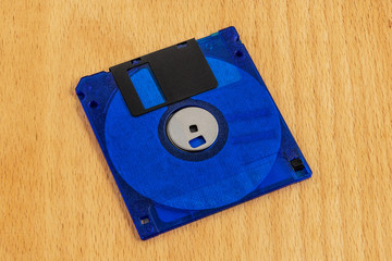 The floppy disk is blue on a wooden background.