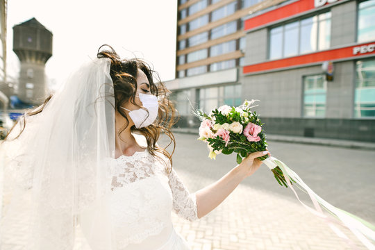 Bride in medical mask on street of city during coronavirus epidemic. Wedding day COVID-19 protection