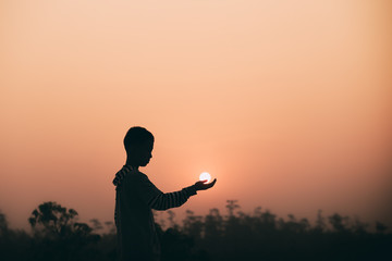 Boy praying to God with sun in hands, worship and thank God, christian silhouette concept.