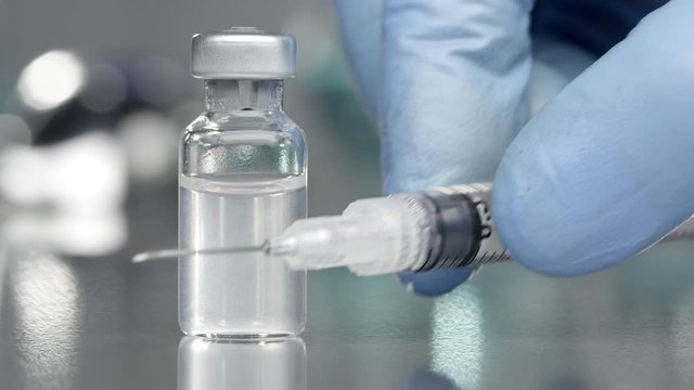 Vial filled with liquid vaccine in medical lab with syringe placed next to it.