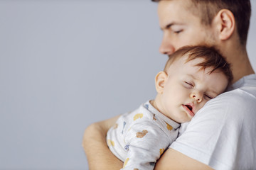 Closeup of adorable little boy sleeping deeply and dreaming while his caring father holding him.