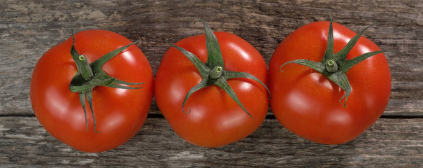 Drei große saftige rote Tomaten (lat.: Solanum lycopersicum) auf rustikalem Holz