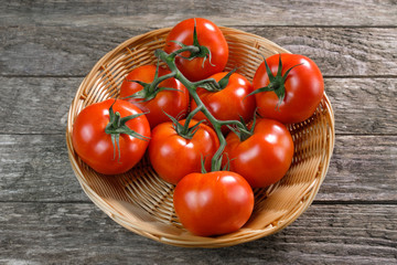 Rote Tomaten (lat.: Solanum lycopersicum) in einem Korb auf rustikalem Holz