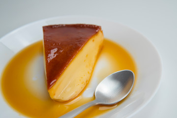 Slice of sugar creamy pudding on white plate with silver spoon.