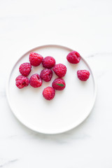Plate of Fresh Raspberries on white marble background with copy space