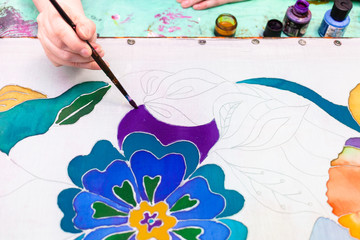 artist draws batik with floral pattern on silk
