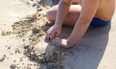 A boy plays in the sand on the beach near the sea.