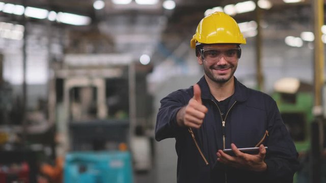 Technician or engineer hold tablet and shows thumbs up to camera while smile with concept of happiness working in factory.