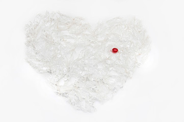 A heart made of transparent candy wrappers with a red candy in the upper right corner. View from above. Isolated