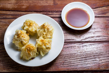 Chinese Steamed Dumpling, Shumai on white dish served with soy sauce on wooden table. Delicious Dimsum pork.