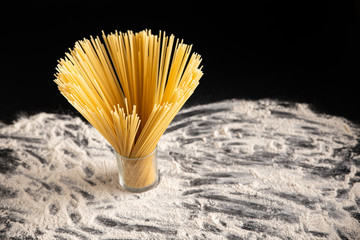 Spaghetti in a glass on a black background. Flour on a black background. 