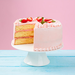 Beautiful layered cake with pink buttercream and fresh strawberry. Colorful background.