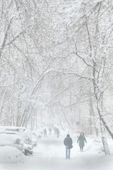 Blizzard in the city. In winter, people walk on a snow-covered road.