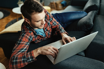 Young man using laptop while relaxing on the sofa at home.