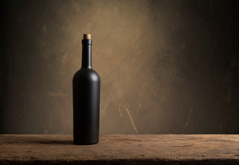 Bartender or male cavist standing near the shelves of wine bottles holds a glass of wine, looks at tint and smells flavor of wine in glass.