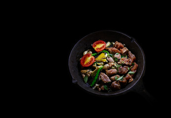Home cooking pork with tomatoes, chili, ginger, garlic in frying pan on black background