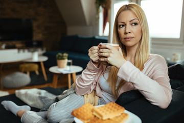 Thoughtful woman having a cup of coffee while relaxing in the living room.