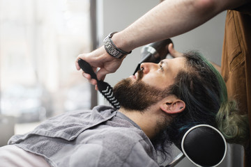 
Barber styling a beard of male customer at barber shop