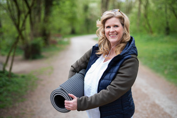 Frau im mittleren Alter ist mit einer Matte freudig auf dem Weg zum Sport 