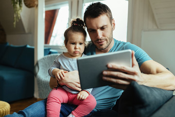 Young father and his daughter using digital tablet in the living room.