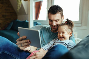Fototapeta premium Happy father and small daughter having fun while using touchpad at home.